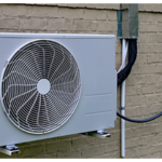A mounted outdoor air conditioning unit is attached to a brick wall, showcasing a neat Mini Split Installation with electrical wiring running to a gray utility box nearby.