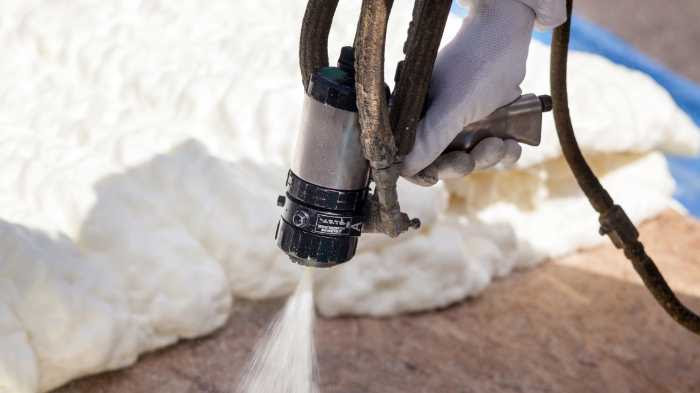 A gloved hand sprays expanding foam insulation onto a surface using a spray gun, showcasing the expertise of Spray Foam Insulation Installers with fresh white foam visible in the background.