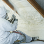 Builder sitting in the attic, spraying the roof above him with foam to seal it