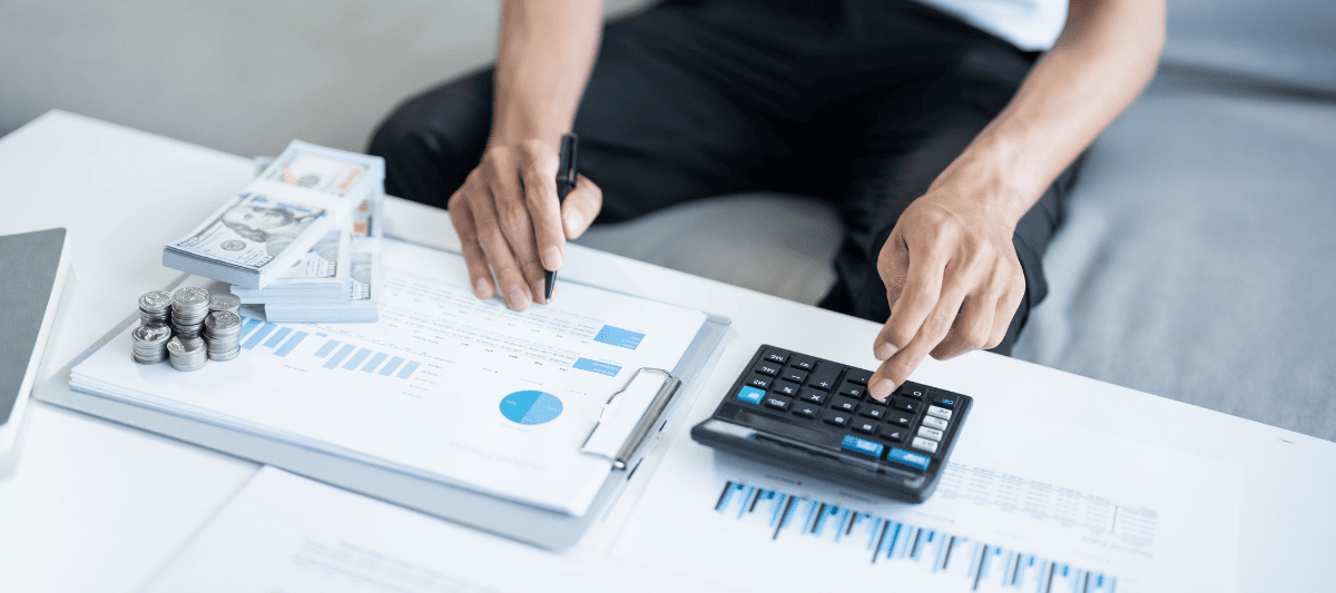 Person calculating home energy savings with calculator, cash and financial documents